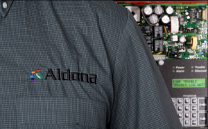 A man in an Aldona Shirt With a fire alarm system in the background